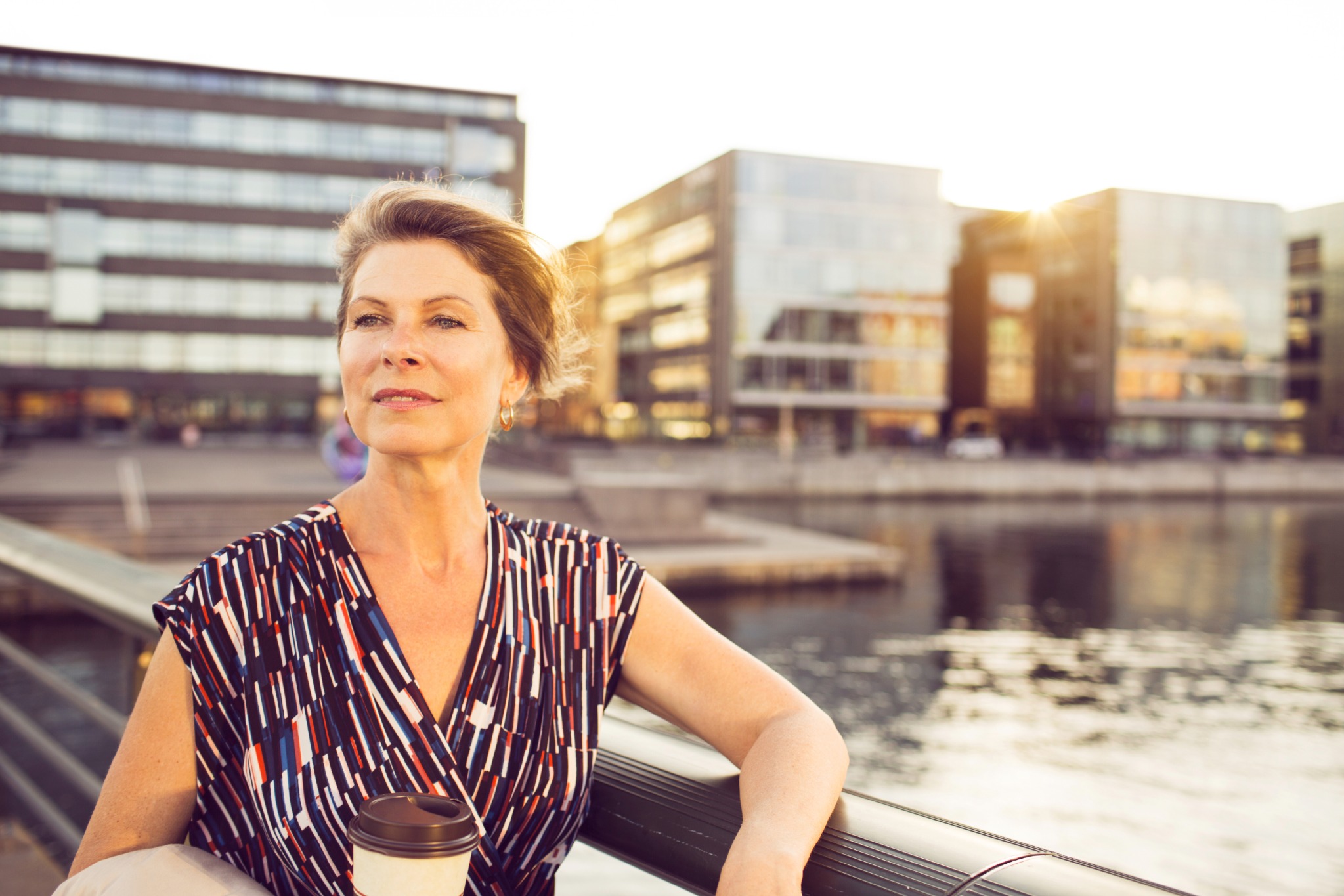 Kvinna med en mugg som vilar på en bänk i staden