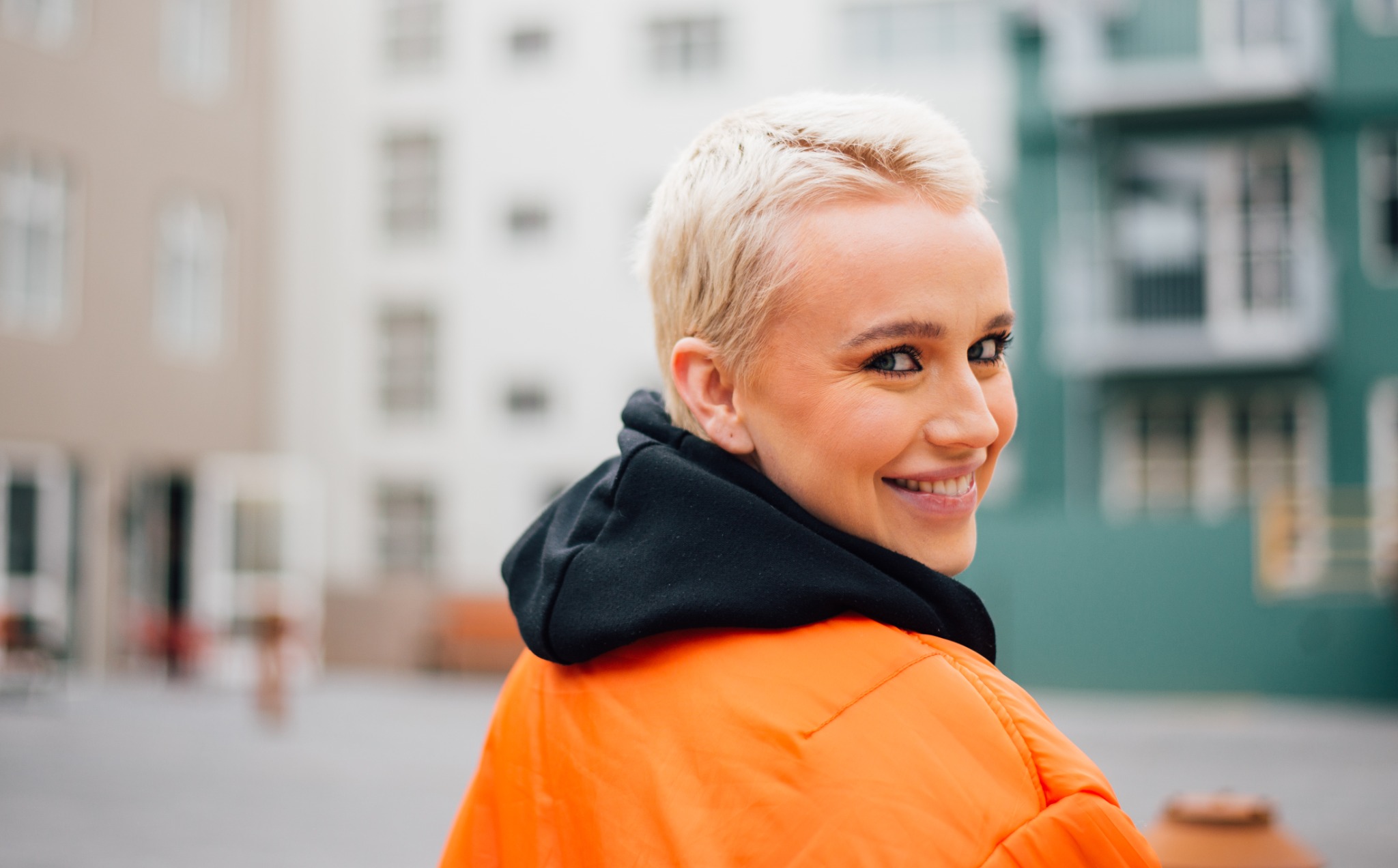 Kvinna med kort, ljust hår och orange jacka